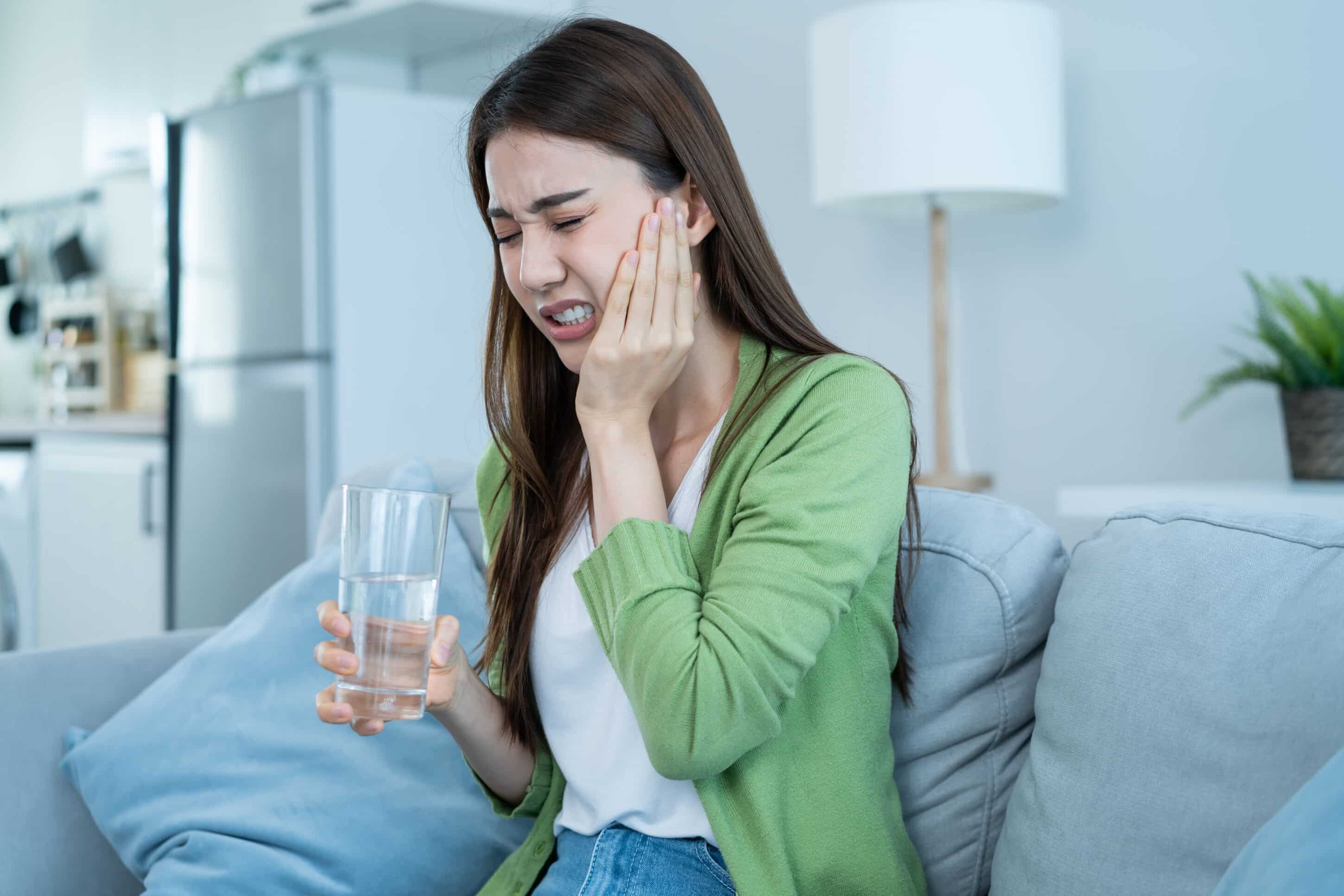 Woman experiencing severe tooth pain and sensitivity while holding her cheek and a glass of water